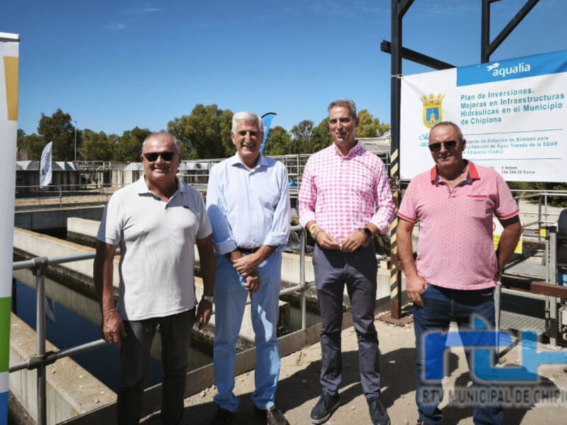 Cuatro personas posan frente a un panel informativo sobre inversiones en infraestructuras municipales, con una bandera de Aguaia y el logo municipal al fondo.