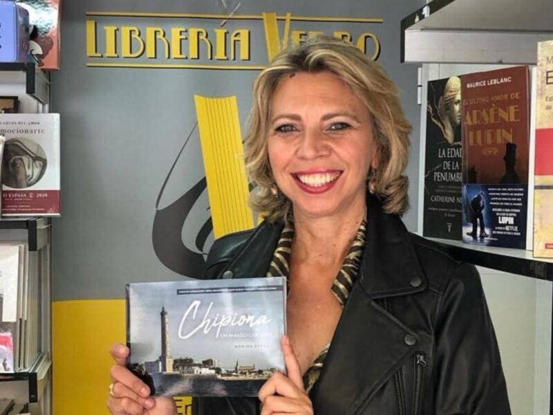 Una mujer sonríe mientras sostiene un libro titulado 'Chipiona' en una librería llamada Librería Vero.
