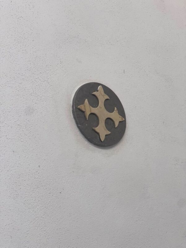 Un símbolo de cruz en forma de corazón, pintado en un tono claro sobre una pared blanca.