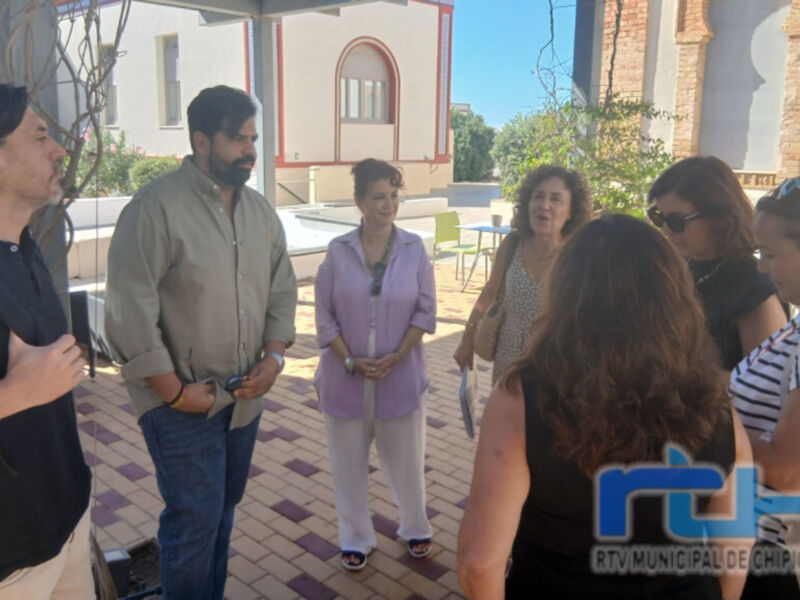Una imagen de una reunión en un patio con varias personas, incluyendo a una mujer en una camisa rosa y pantalones beige. La escena parece ser un evento o reunión formal, posiblemente en una oficina o centro de trabajo.