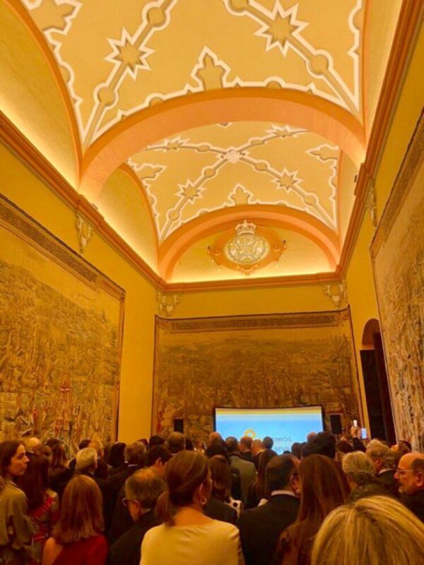 Salón con techo decorado, muro con relieve y pantalla de proyección en el fondo.