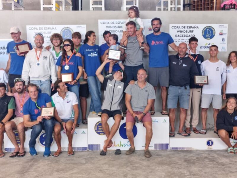 Copa de España de Triatlón, celebración en la playa. Ganadores posan con medallas y trofeos. Bandera de FENI y logotipo de AECOPA en el fondo.