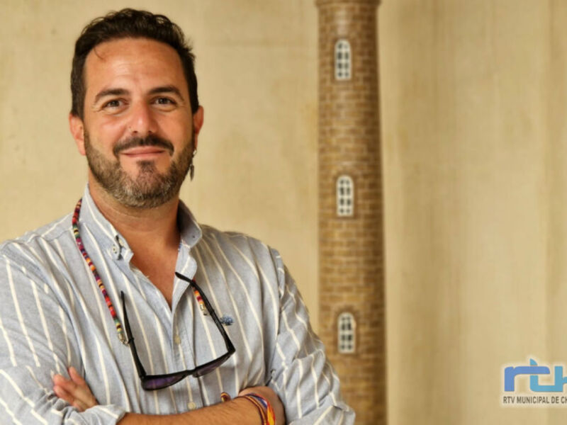 Un hombre con barba y gafas de sol, posando frente a un edificio histórico.