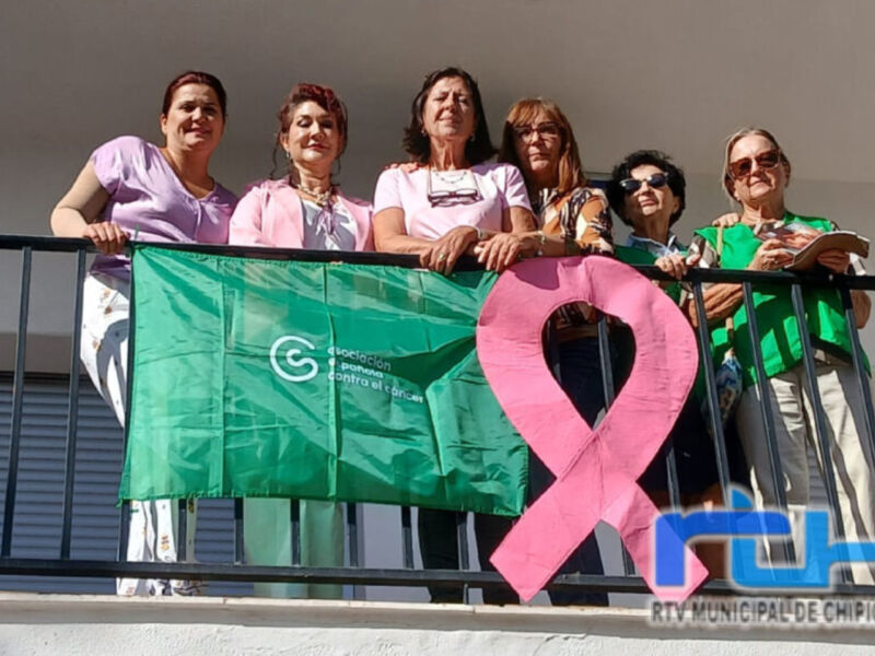Una grupo de personas con una bandera verde y rosa en forma de cinta, posiblemente simbólica para la lucha contra el cáncer.
