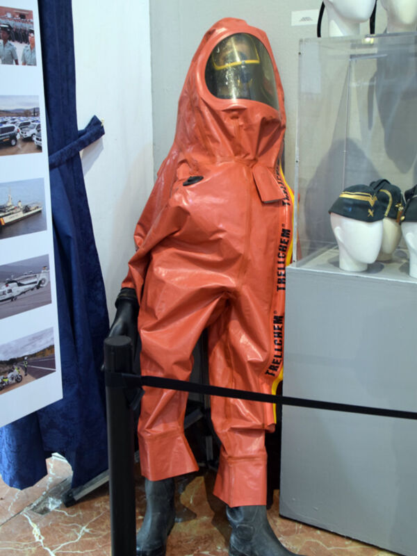Un traje de protección rojo con casco y botas negras, colocado en un estante junto a otros equipamientos de seguridad.