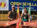 Dos tenistas posan con sus trofeos en el Open Sevilla, con banderas y un cartel de premios.