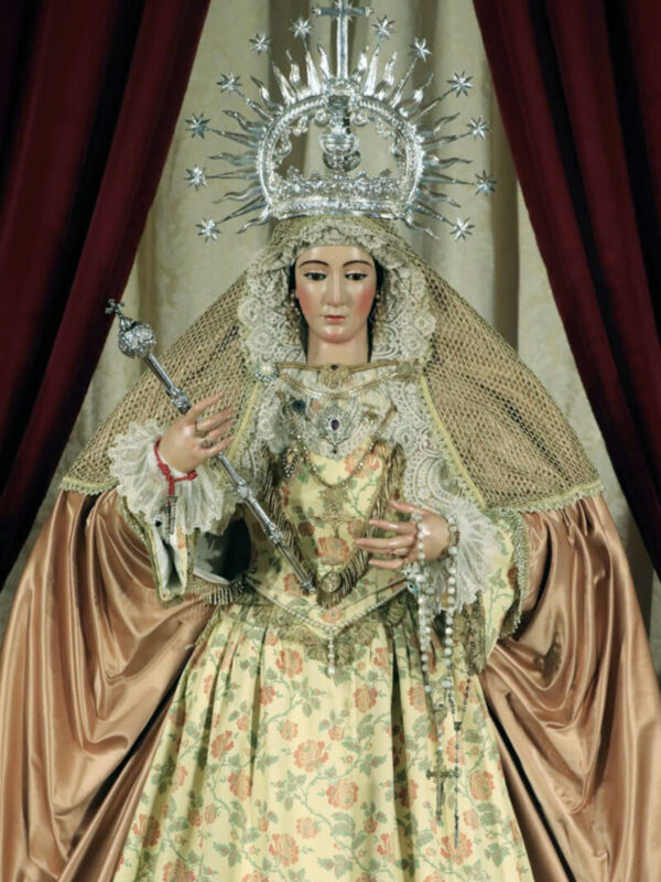 Imagen de una Virgen con vestimenta tradicional y coronada, posiblemente en un altar o espacio religioso.