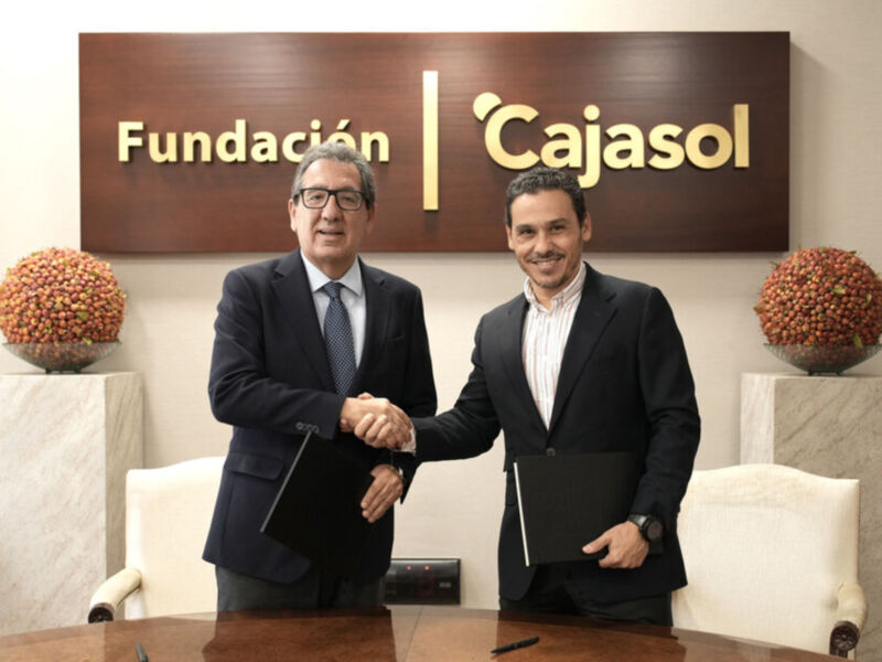 Dos hombres en trajes se estrechan la mano frente a una pared con el letrero "Fundación Cajasol". Ambos están en un entorno formal, posiblemente una oficina o sala de conferencias.