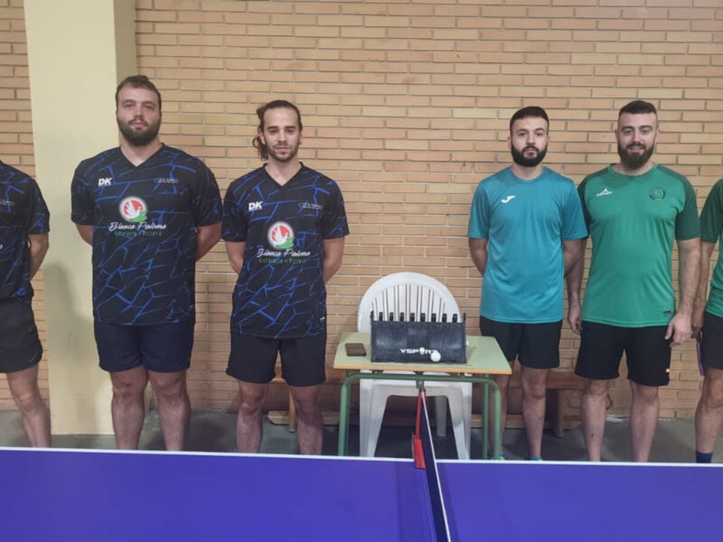 Los jugadores de tenis de mesa posan frente a su mesa en un entorno deportivo.