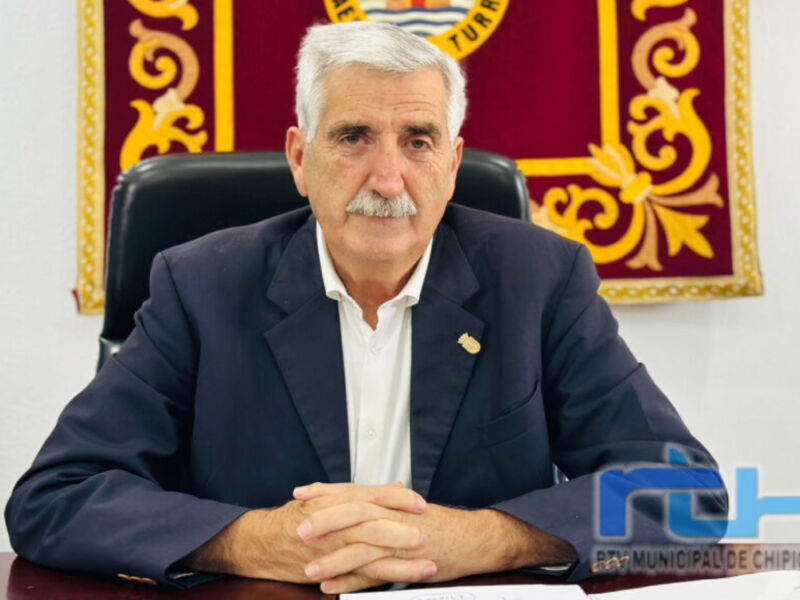 El presidente de la Junta de Andalucía, Juan Manuel Moreno Bonilla, es el protagonista en esta imagen. Se encuentra sentado en un escritorio con una bandera de Andalucía al fondo, lo que indica su posición oficial. Moreno Bonilla es conocido por su liderazgo en la política regional y sus compromisos con el desarrollo económico y social de Andalucía.