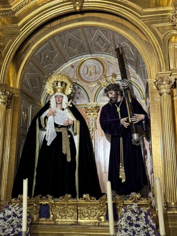 Estas estatuas religiosas se encuentran en un altar dorado con detalles geométricos, flanqueadas por columnas y adornadas con flores. La estatua de la izquierda lleva un manto negro y una corona dorada, mientras que la de la derecha sostiene un instrumento musical. La arquitectura dorada y el altar reflejan la belleza y solemnidad de esta iglesia.