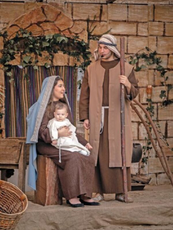 Imagen de una escena navideña con un hombre y una mujer vestidos tradicionalmente, posiblemente representando a José y María con el bebé Jesús. El fondo muestra una estructura de madera, típica de un pesebre navideño.