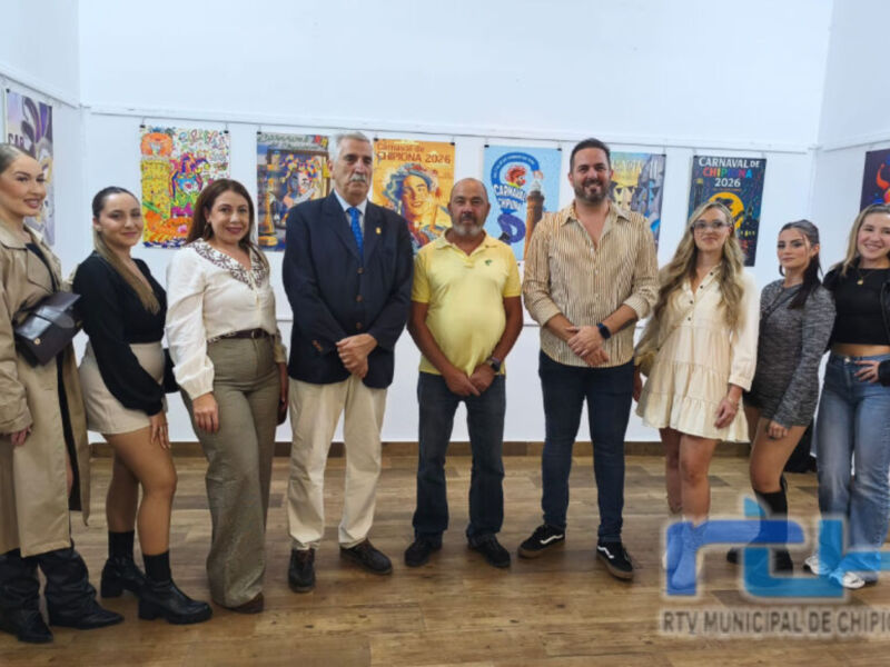 Grupo de personas posando en una exposición de carteles, con un fondo blanco y varias obras de arte colgadas.