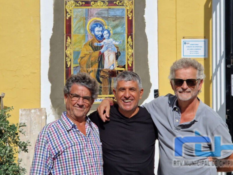 Tres hombres sonrientes frente a una imagen religiosa y una placa con información.
