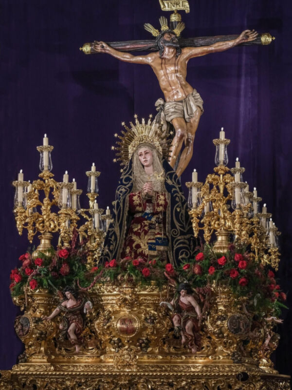 Imagen de Cristo crucificado en un altar dorado, rodeado por flores rojas y esculturas de ángeles.