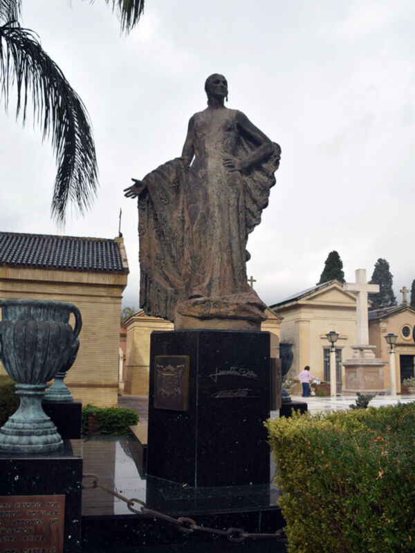 La estatua de un personaje histórico en una tumba con un pedestal negro, rodeada por vegetación y otros monumentos.