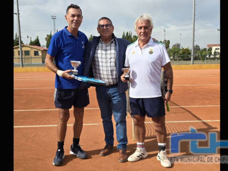 Tres personas posan con trofeos en una cancha de tenis. El ambiente es festivo, indicando un torneo o competición deportiva.
