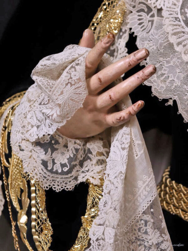 Una mano con guantes de encaje blanco y detalles dorados, posando sobre una falda de encaje.