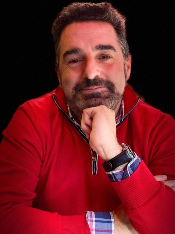 Un hombre con una camisa roja y un chaleco de cuadros azules, mirando directamente a la cámara.